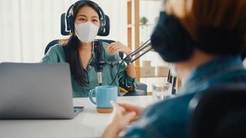 Asia girl radio host record podcast use microphone wear headphone interview guest content wear mask protect virus conversation talk and listen in her room. Podcast from home, coronavirus quarantine. photo