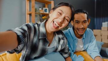 Happy young asian couple man and woman sit couch use looking at camera video call with friends and family in living room at home. Stay at home quarantine, Social distancing, Young married concept. photo