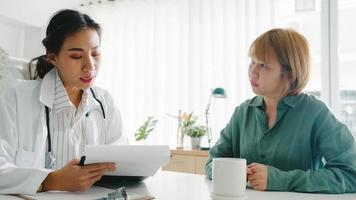 Young Asia female doctor in white medical uniform using clipboard is delivering great news talk discuss results or symptoms with girl patient sitting at desk in health clinic or hospital office. photo
