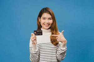 Young Asia lady show credit bank card with positive expression, smiles broadly, dressed in casual clothing feeling happiness and stand isolated on blue background. Facial expression concept. photo