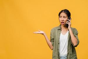 Young Asia lady talk by phone with negative expression, excited screaming, cry emotional angry in casual cloth and stand isolated on yellow background with blank copy space. Facial expression concept. photo