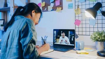 Asia empresaria usando laptop hablar con colegas sobre el plan en la reunión de videollamada en la sala de estar. trabajando desde casa por sobrecarga nocturna, trabajo a distancia, distanciamiento social, cuarentena por coronavirus.