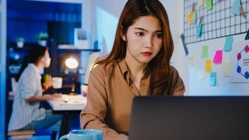 Happy Asia businesswoman social distancing in new normal situation for virus prevention while using laptop online business overtime back at work in office night. Life and work after coronavirus. photo