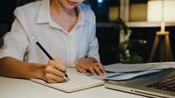 Señora independiente de Asia que usa el trabajo duro de la computadora portátil en la sala de estar de la casa. trabajo desde casa sobrecarga por la noche, trabajo a distancia, autoaislamiento, distanciamiento social, cuarentena para la prevención del virus corona. foto