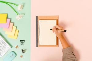 Creative flat lay photo of workspace desk. Top view office desk with keyboard, mouse and open mockup black notebook on pastel green pink color background. Top view mock up with copy space photography.