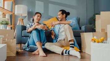 Happy asian young attractive couple man and woman sit at new home drink coffee relax and talk smile with carton package box storage to move in new house. Young married asian move home concept. photo