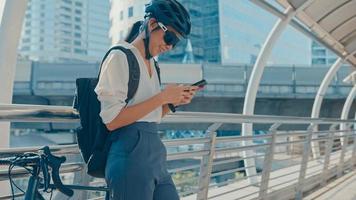 Happy asian businesswoman with backpack use smart phone in city stand at street with bike go to work at office. Sport girl use her phone for working job. Commute to work, Business commuter in city. photo