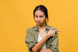 Young Asia Lady shows something amazing at blank space with negative expression, excited screaming, crying emotional angry looking at camera isolated over yellow background. Facial expression concept.