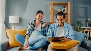 Happy asian young attractive couple man and woman sit on couch use tablet shopping online furniture decorate home in the living room at new house. Young married moving home shopper online concept. photo