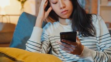 Thoughtful Asia lady holding phone feeling sad waiting for call sit at sofa in living room at house night feel lonely, Sad depressed teenager spend time alone, Social distance, Coronavirus quarantine. photo