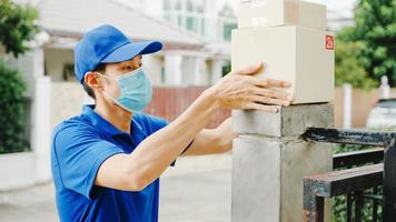 Young postal delivery courier man wear face mask handling parcel box for send to customer at house and Asian female receive delivered package outdoors. Lifestyle new normal after corona virus concept. photo