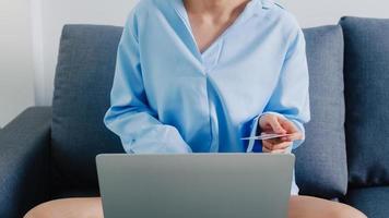 Young Asia lady using laptop, credit card buy and purchase e-commerce internet in living room at house. Stay at home, online shopping, self isolation, social distancing, quarantine for coronavirus. photo