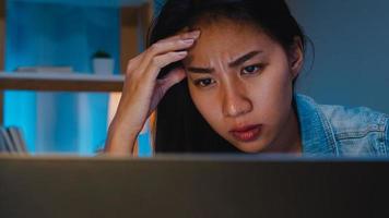 Millennial young Chinese businesswoman working late night stress out with project research problem on laptop in living room at modern home. Asia people occupational burnout syndrome concept. photo