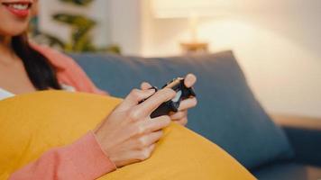 Young Asia lady using wireless controller play video game having funny happy moment on sofa in living room at home night. Stay at house, Self quarantine activity for covid or coronavirus quarantine. photo