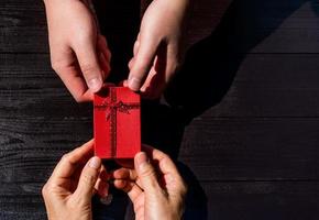 Young people give red present box to senior woman during christmas and new year celebration. wooden background with copy space photo