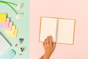 Creative flat lay photo of workspace desk. Top view office desk with keyboard, mouse and open mockup black notebook on pastel green pink color background. Top view mock up with copy space photography.