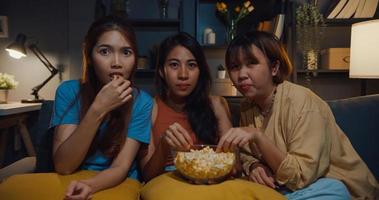 Group of attractive Asia lady girl freaking out fear and terrified moment eat popcorn watch horror online movie on couch in living room at home in night. Weekend lifestyle activity quarantine concept. photo