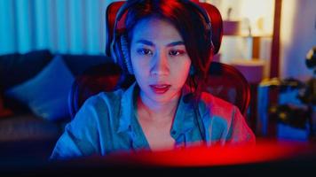 Close-up face happy asia professional girl gamer wear headphone competition play video game neon light computer in living room at home. Esport streaming game online, Home quarantine activity concept. photo