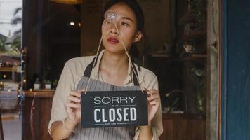 Young Asia manager girl turning a sign from open to closed sign on glass door cafe after coronavirus lockdown quarantine. Owner small business, food and drink, business financial crisis concept. photo