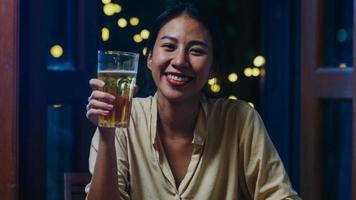 Young Asia lady drinking beer having fun happy night party New Year event online celebration via video call by phone at home at night. Social distance, quarantine for coronavirus. Point of view or POV photo