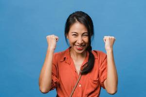 Young Asia lady with positive expression, joyful and exciting, dressed in casual cloth and look at camera over blue background. Happy adorable glad woman rejoices success. Facial expression concept. photo