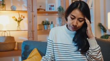 Thoughtful Asia lady suffering from insomnia sit at sofa in living room at house night with feel lonely, Sad depressed teenager spend time alone stay at home, Social distance, Coronavirus quarantine. photo