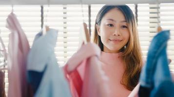 Beautiful attractive young Asia lady choosing her fashion outfit clothes in closet at house or store. Girl think what to wear casual shirt. Home wardrobe or clothing shop changing room. photo