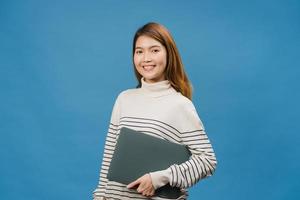 Surprised young Asia lady hold laptop with positive expression, smile broadly, dressed in casual clothing and looking at camera on blue background. Happy adorable glad woman rejoices success. photo