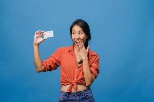 Young Asia lady show credit bank card with positive expression, smiles broadly, dressed in casual clothing feeling happiness and stand isolated on blue background. Facial expression concept. photo