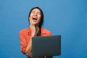 Young Asia lady using laptop with positive expression, smiles broadly, dressed in casual clothing feeling happiness and stand isolated on blue background. Happy adorable glad woman rejoices success. photo