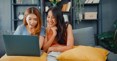 Two Asia lesbian women site on couch together looking at laptop screen in living room at home together. Happy couple roommate ladies enjoy web surfing online shopping, Lifestyle woman at home concept. photo