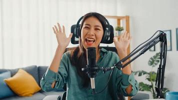 Happy asia girl record a podcast with headphones and microphone look at camera  talk and take a rest in her room. Female podcaster make audio podcast from her home studio, Stay at house concept. photo
