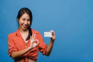 Young Asia lady show credit bank card with positive expression, smiles broadly, dressed in casual clothing feeling happiness and stand isolated on blue background. Facial expression concept. photo