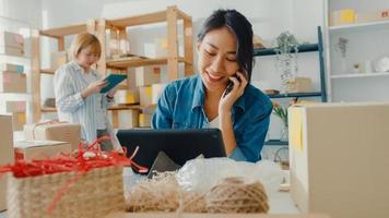 Young Asia businesswomen using mobile phone call receiving purchase order and check product on stock work at home office. Small business owner, online market delivery, lifestyle freelance concept. photo