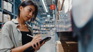 Attractive young Asia businesswoman manager looking for goods using digital tablet checking inventory levels standing in retail shopping center. Distribution, Logistics, Packages ready for shipment. photo