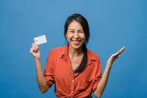 Young Asia lady show credit bank card with positive expression, smiles broadly, dressed in casual clothing feeling happiness and stand isolated on blue background. Facial expression concept. photo