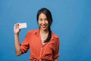 Young Asia lady show credit bank card with positive expression, smiles broadly, dressed in casual clothing feeling happiness and stand isolated on blue background. Facial expression concept. photo