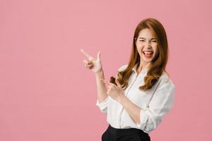 Retrato de joven asiática sonriendo con expresión alegre, muestra algo sorprendente en el espacio en blanco en ropa casual y mirando a cámara aislada sobre fondo rosa. concepto de expresión facial.