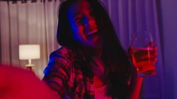 Young Asia lady drinking beer having fun happy moment disco neon night party event online celebration via video call in living room at home. Social distancing, quarantine for coronavirus prevention. photo