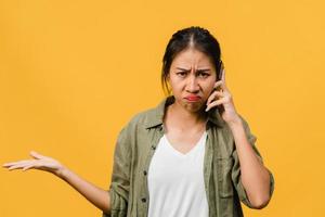 jovencita asiática habla por teléfono con expresión negativa, gritos emocionados, gritos emocionales enojados en ropa casual y se para aislado sobre fondo amarillo con espacio de copia en blanco. concepto de expresión facial. foto