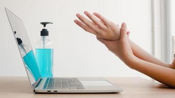 Mujer asiática que usa alcohol gel desinfectante lavarse las manos antes de trabajar en la computadora portátil para proteger el coronavirus. Las mujeres empujan el alcohol para limpiar por higiene cuando el distanciamiento social se queda en casa y el tiempo de auto cuarentena.