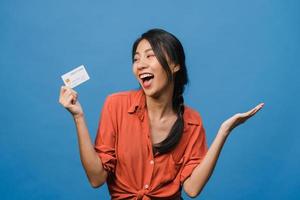 Young Asia lady show credit bank card with positive expression, smiles broadly, dressed in casual clothing feeling happiness and stand isolated on blue background. Facial expression concept. photo