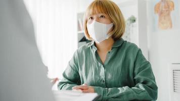 Young Asia lady doctor wear protective mask using clipboard is delivering great news talk discuss results or symptoms with girl patient in hospital office. Lifestyle new normal after corona virus. photo