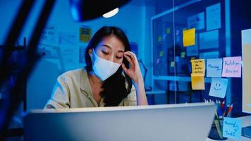 Las mujeres asiáticas independientes usan mascarilla usando una computadora portátil en el trabajo duro en la nueva oficina normal. trabajo desde casa sobrecarga nocturna, autoaislamiento, distanciamiento social, cuarentena para la prevención del virus corona.