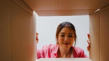 Excited Asian young woman unpack opening huge carton box and looking inside new gift at home. Happy millennial female client satisfied with ordered purchase. Delivery and online shopping concept. photo