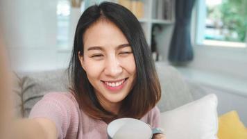Young Asian teenager woman vlog at home, female drinking coffee and using smartphone making vlog video to social media in living room. Lifestyle woman relax in morning at home concept. photo