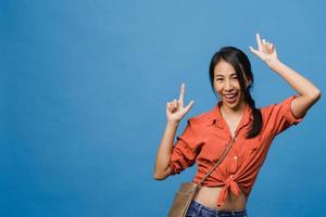 Portrait of young Asian lady smiling with cheerful expression, shows something amazing at blank space in casual cloth and looking at camera isolated over blue background. Facial expression concept. photo