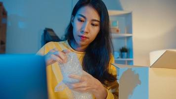 Young Asia businesswoman packing glass use bubble wrap for packing support damage fragile product in home office at night. Small business owner, online market delivery, lifestyle freelance concept. photo