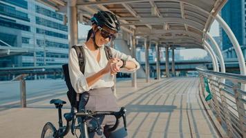 Asian businesswoman with backpack bicycle smiling look smartwatch in city street go to work at office. Sports girl use her watch app for fitness tracking. Commute to work, Business commuter in city. photo