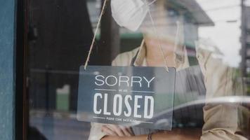 Young Asia girl wear face mask turning a sign from open to closed sign on glass door cafe after coronavirus lockdown quarantine. Owner small business, food and drink, business financial crisis concept photo